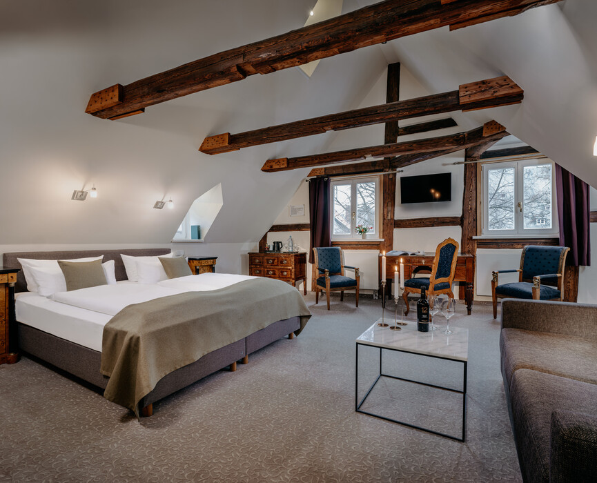 Großzügiges Zimmer unter dem Dach mit sichtbaren Holzbalken und gemütlicher Sitzecke.