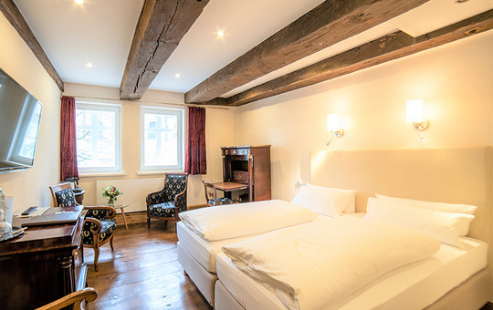 Weiß bezogenes Doppelbett, Sekretär und zwei gemütliche Stühle in einem der Hotelzimmer in Goslar.