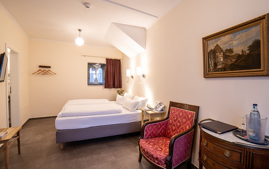 Ein Doppelbett mit Nachtkästchen, rotem Stuhl und Kommode in einem der Hotelzimmer in Goslar.