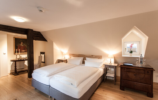 Weiß bezogenes Doppelbett mit zwei Nachttischen und Kommode in einem der Hotelzimmer in Goslar.