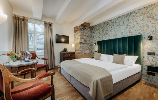 Gemütliches Doppelzimmer mit floraler Tapete und Sitzecke.