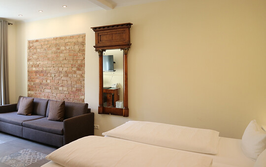 Blick in eines der Hotelzimmer in Goslar mit Doppelbett, hölzernem Spiegel und Sofa.