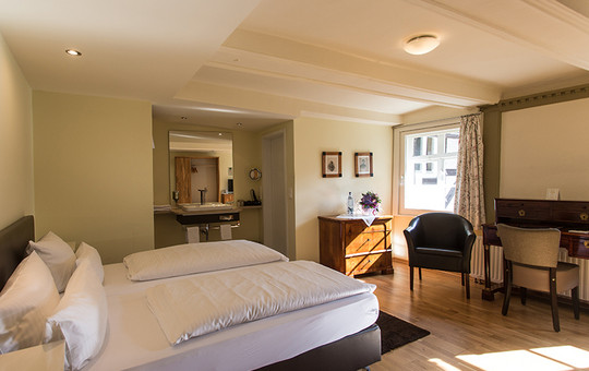 Mascaroden hotel room in Goslar with large bed, seating and view of the bathroom.
