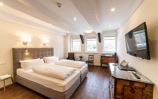 Superior Hotelzimmer in Goslar mit großem Doppelbett, zwei Stühlen mit Beistelltisch und Fernseher.
