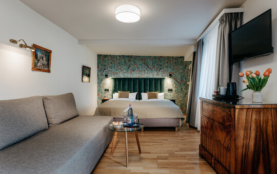 Komfortables Zimmer mit Couch, Fernseher und floralem Wandmotiv.